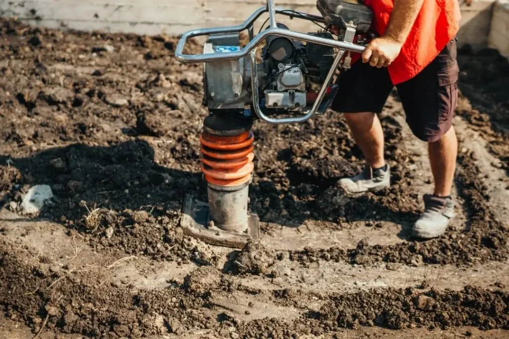 Worker using a tamper to compact soil